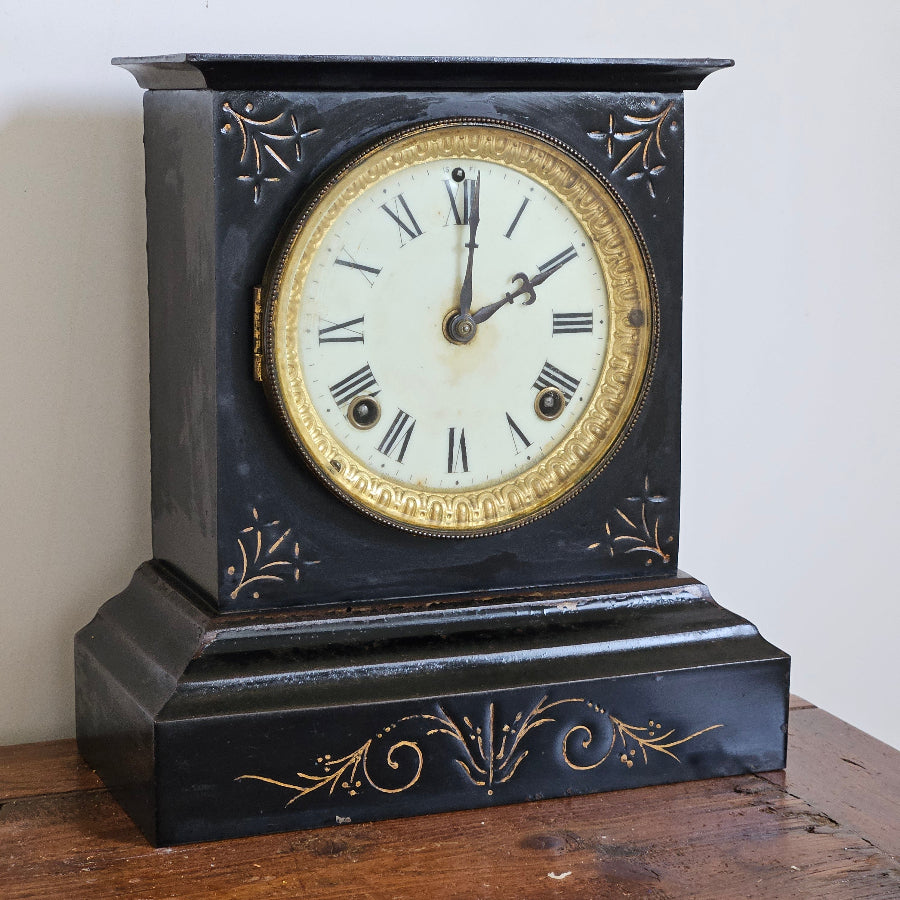 Vintage wall clock with black and gold decorative case on a white wall.